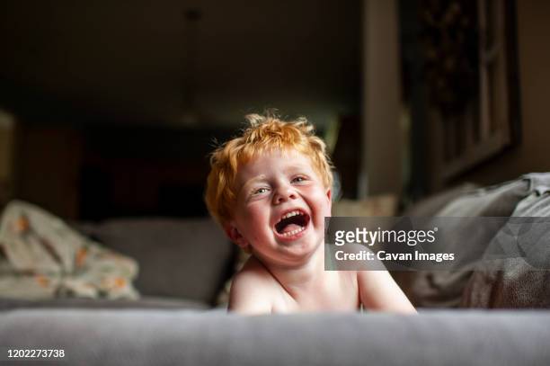 toddler boy with red hair laughing while laying on couch at home - funny baby faces stock pictures, royalty-free photos & images