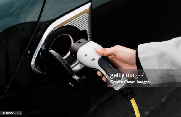 woman's hand plugging in a charger in an electric car socket - electric car charger imagens e fotografias de stock