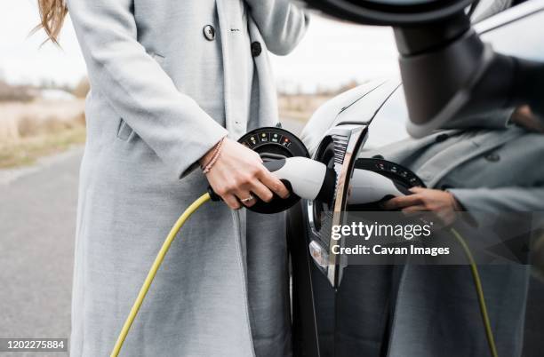 view of woman's hand plugging in charging lead to her electric car - elektrische auto stockfoto's en -beelden