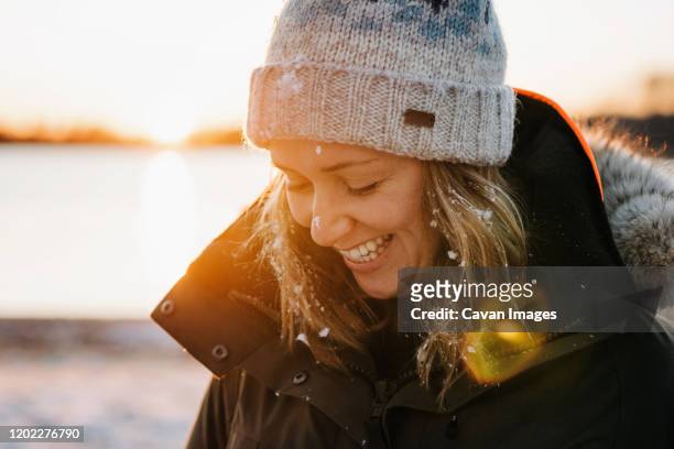 portrait of woman laughing with snow in her hair in winter at sunset - face snow stockfoto's en -beelden