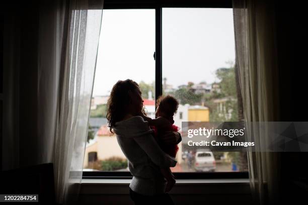 late thirties mother holding baby in front of window for silouette - blended family stockfoto's en -beelden
