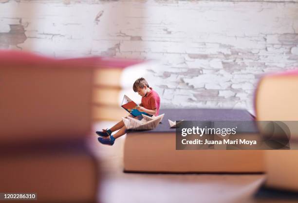 little boy reading about a big book.  around there are several giant books.  conceptual photography - children's literature stock pictures, royalty-free photos & images
