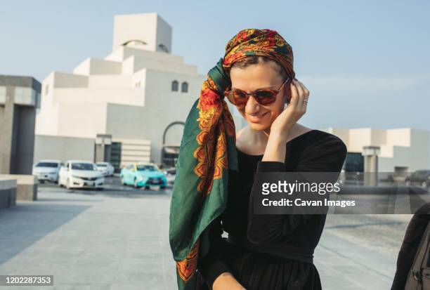 young woman with headwrap smiling and looking down - tour of qatar fotografías e imágenes de stock