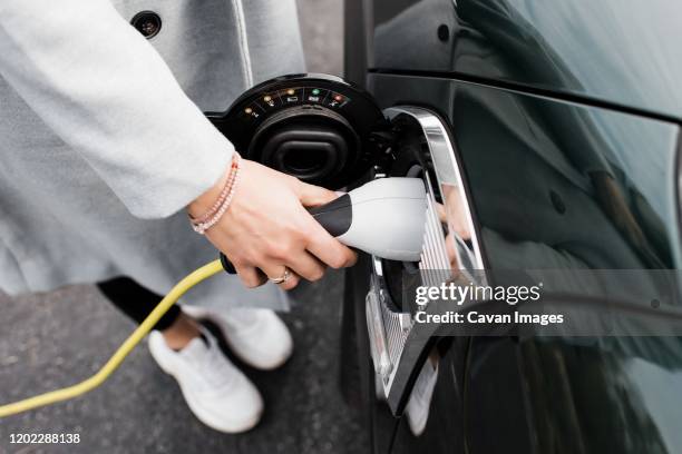 woman's hand plugging in a charging lead to her electric car - hybrid car stockfoto's en -beelden