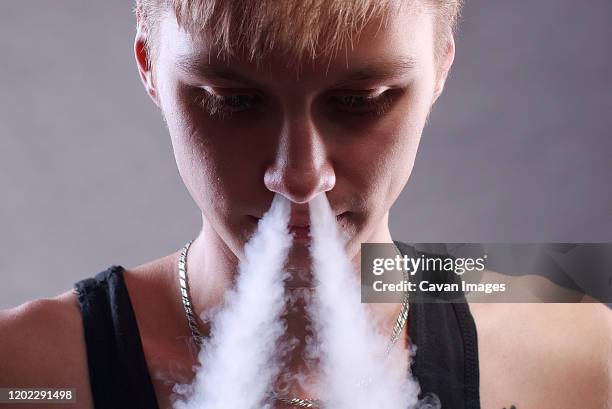 young man white smoke nose over grey background - boys smoking cigarettes stock pictures, royalty-free photos & images