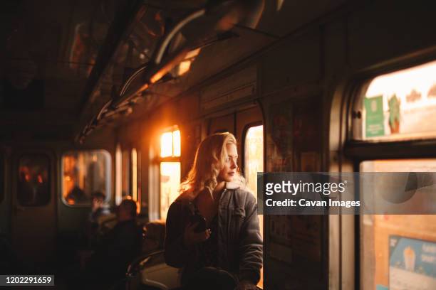 young woman looking through window traveling in subway train - goldene stunde stock-fotos und bilder