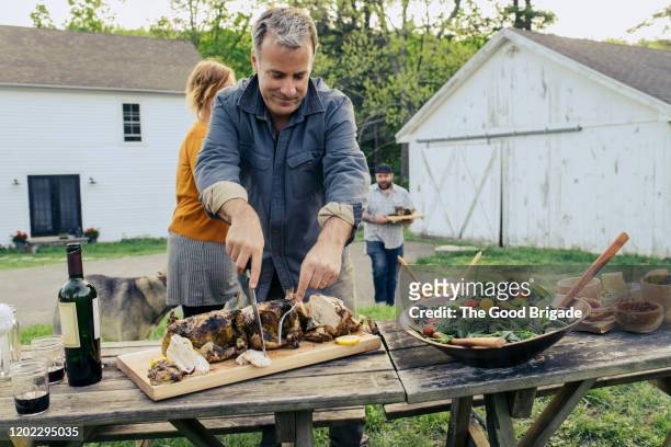 man carving chicken at table outdoors - bbq chicken stock-fotos und bilder