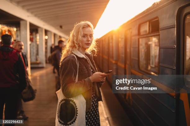 young woman with smart phone standing at subway station - white collar worker dawn light stock pictures, royalty-free photos & images