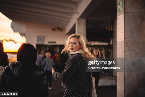 young woman looking back at camera walking on subway station - going home night stock-fotos und bilder