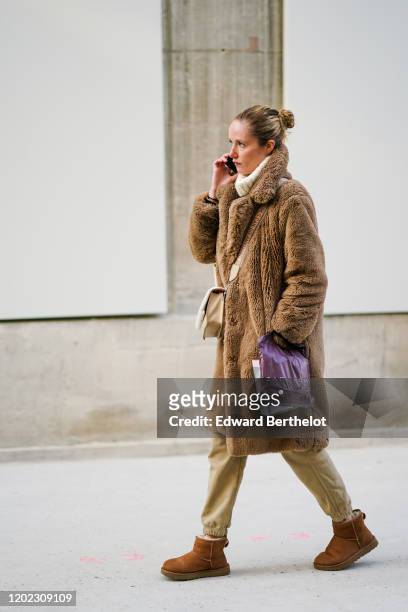 Guest wears a brown winter faux fur fluffy coat, beige pants, brown shoes, a white wool turtleneck pullover, a bag, outside Maison Margiela, during...