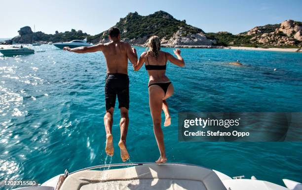 young couple jumping into sea from yacht, la maddalena island, sardegna, italy - jumping of boat foto e immagini stock
