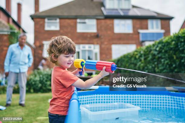 boy playing with water gun by pool - plastic pool stockfoto's en -beelden