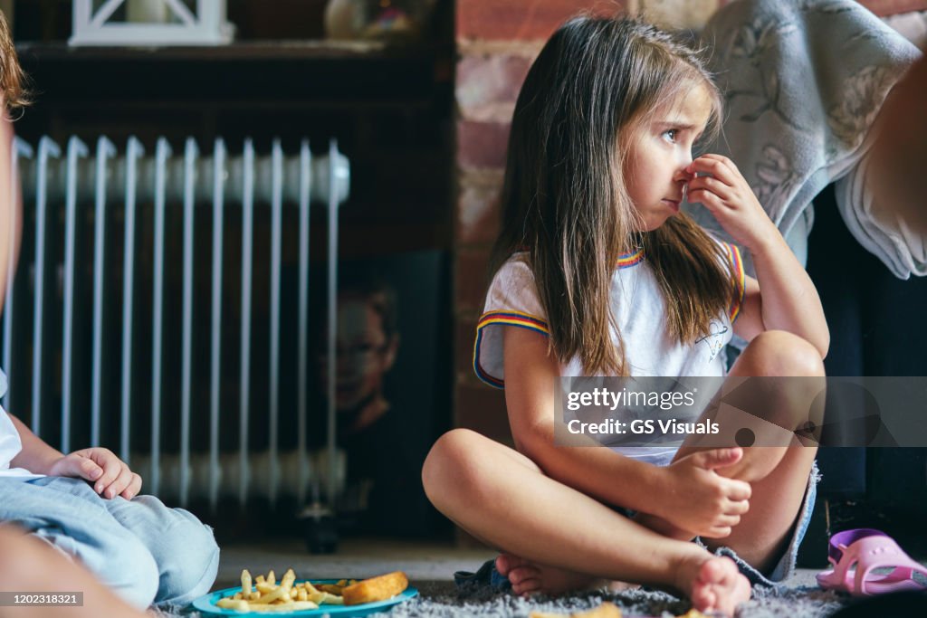 Girl sitting on rug beside radiator scratching nose