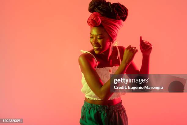 woman with headscarf dancing against peach background - dans kleur stockfoto's en -beelden