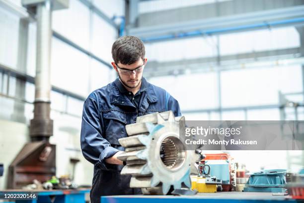 apprentice engineer cleaning gear for pump in electrical engineering factory - engineer gearwheel factory stock pictures, royalty-free photos & images
