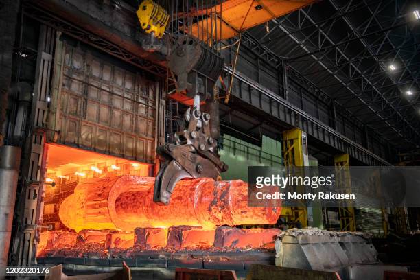 heat treated red hot steel ingot being lifted by crane in furnace in steelworks - steel mill stock pictures, royalty-free photos & images