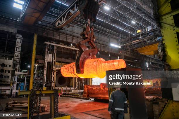 red hot steel ingot being craned to forge in steelworks - smederij stockfoto's en -beelden