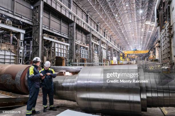 workers inspecting large steel roller in forge of steelworks - staal fabriek stockfoto's en -beelden