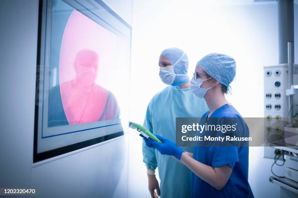 nurse and surgeon inspecting screens in operating theatre in hospital setting - operatiegewaad stockfoto's en -beelden