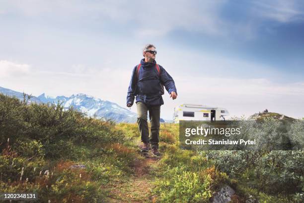 Senior man traveling with backpack, campervan and mountains in background