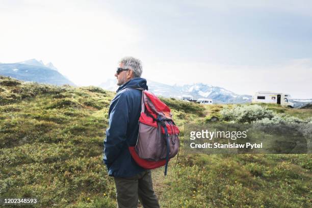 senior man traveling with backpack in mountains - grass looking distance stock-fotos und bilder
