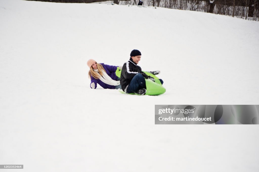 Generation Z couple sliding down in snowy public park.