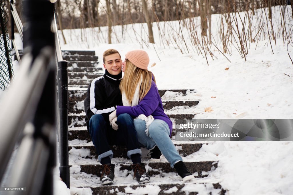 Pareja de generación Z descansando en la escalera nevada del parque público en invierno.