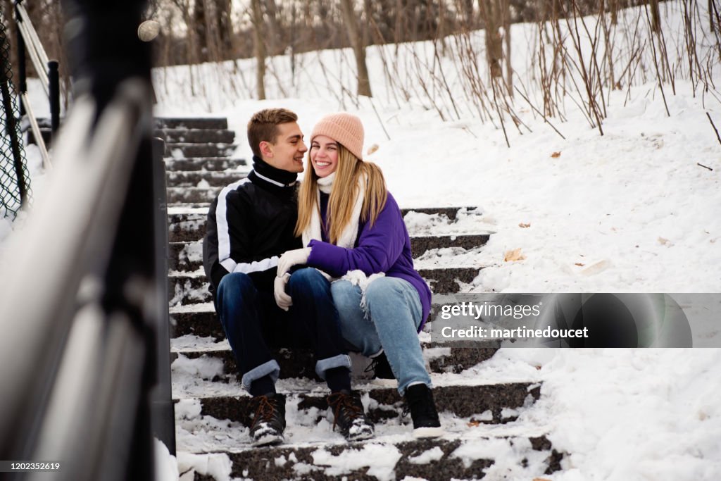 Pareja de generación Z descansando en la escalera nevada del parque público en invierno.