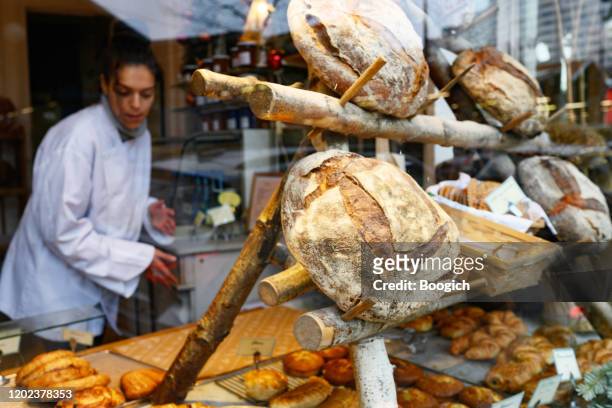 female chef can be seen working behind the fresh bread in a bakery window paris france - boulangerie paris stock pictures, royalty-free photos & images