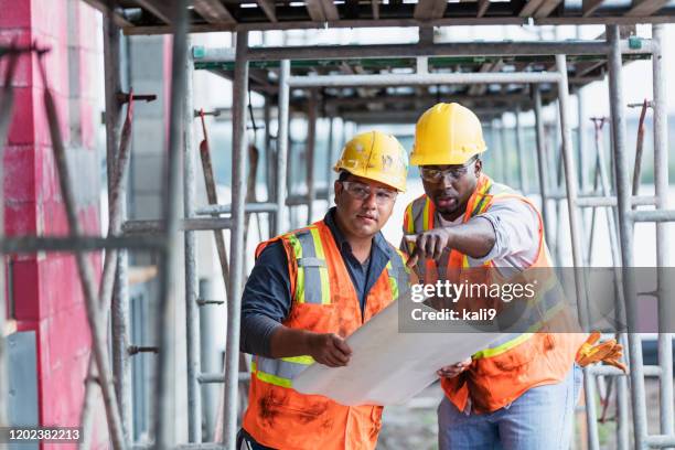 workers at construction site looking at plans, pointing - hispanic construction worker stock pictures, royalty-free photos & images