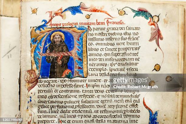 detail of opening text page of illuminated manuscript, showing initial drop capital illustration of st francis of assisi, with decorative marginalia. - st francis stock pictures, royalty-free photos & images