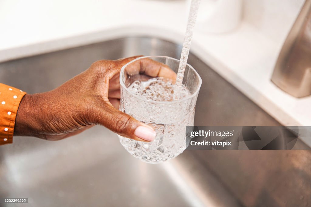 Vertiendo un poco de agua del grifo en su vaso