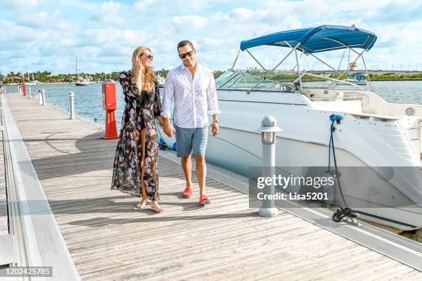 beautiful adult couple in swimwear on a dock on the ocean with speedboat yacht luxury and idyllic location - florida marina stock pictures, royalty-free photos & images