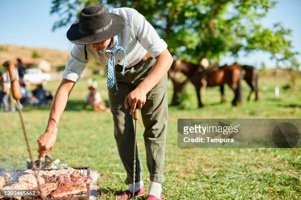 young gaucho grilling meat in the traditional argentinian way. - argentina traditional food stock pictures, royalty-free photos & images