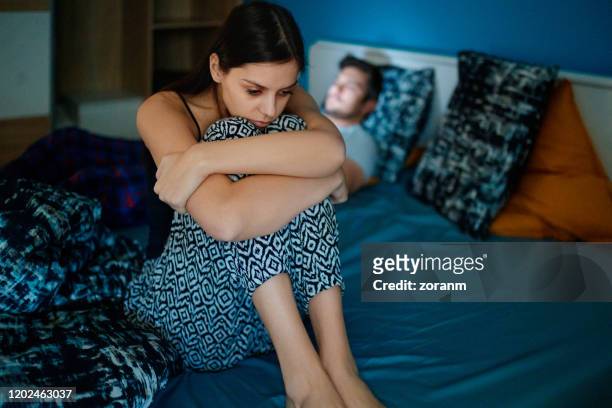 droevige vrouwenzitting op bed met partner op achtergrond - vechten stockfoto's en -beelden