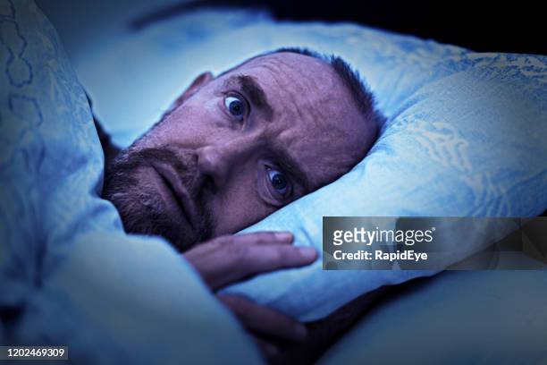 ベッドに横たわっている成熟した男は、広い目を覚まし、心配して怖がって見えます - terrified ストックフォトと画像