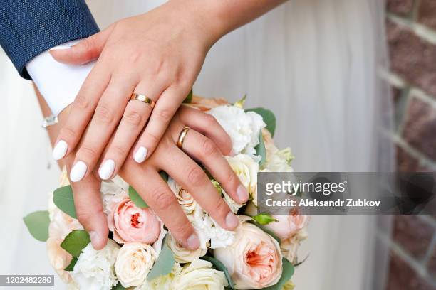 hands of the bride and groom on the wedding bouquet. - coniugi foto e immagini stock