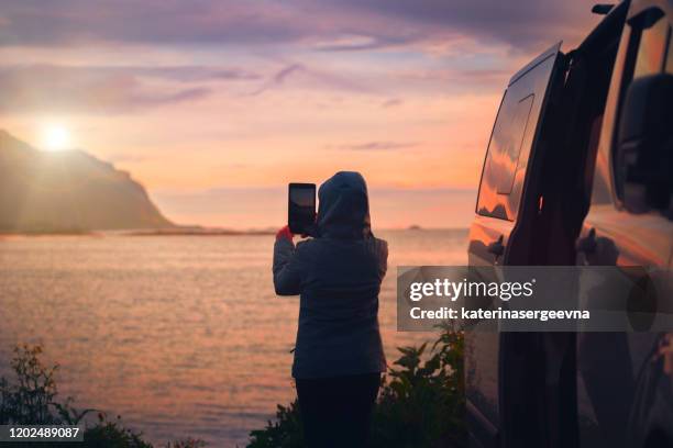 vrouw bij de auto fotografeert de zonsondergang op de zee - auto tablet stockfoto's en -beelden