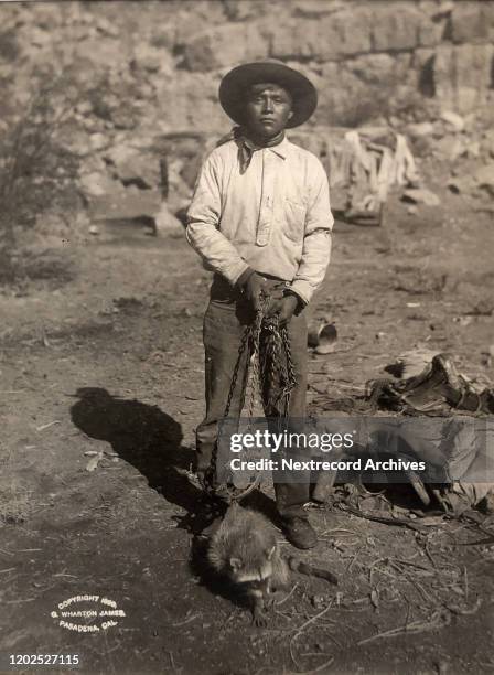 Vintage portrait taken 1899 by George Wharton James of indigenous Havasupia tribe man holding chained captive raccoon, taken in Pasadena, California,...