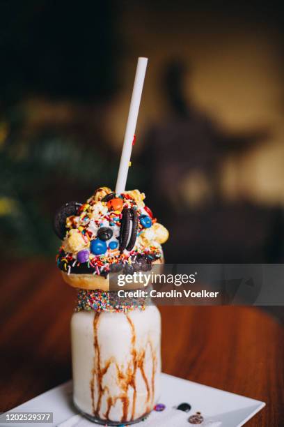 chocolate donut milkshake with lots of toppings, sprinkles, popcorn, cookies and cream standing on a wooden table - straw ストックフォトと画像