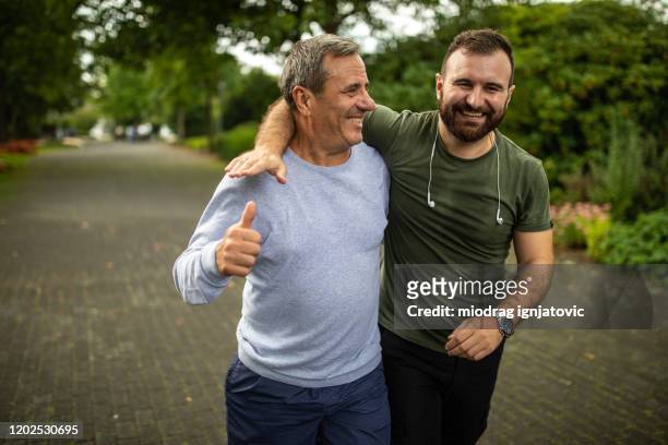 mature man and his son jogging in park on autumn morning - mid adult stock pictures, royalty-free photos & images
