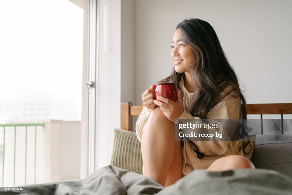 Schöne junge Frau trinken heißes Getränk in ihrem Bett am Morgen