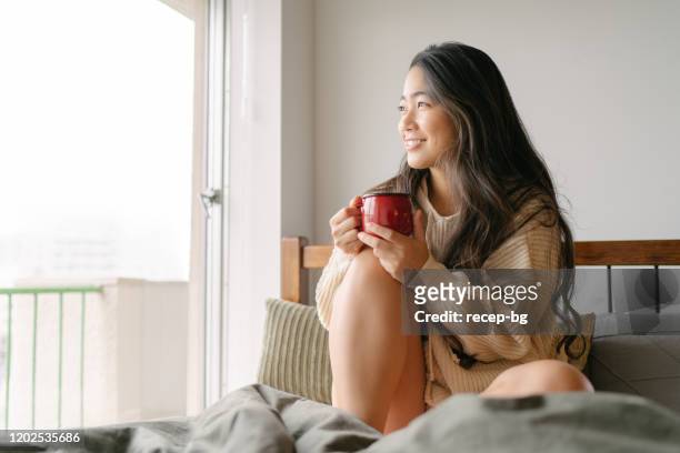 hermosa joven bebiendo bebida caliente en su cama en la mañana - despertar fotografías e imágenes de stock