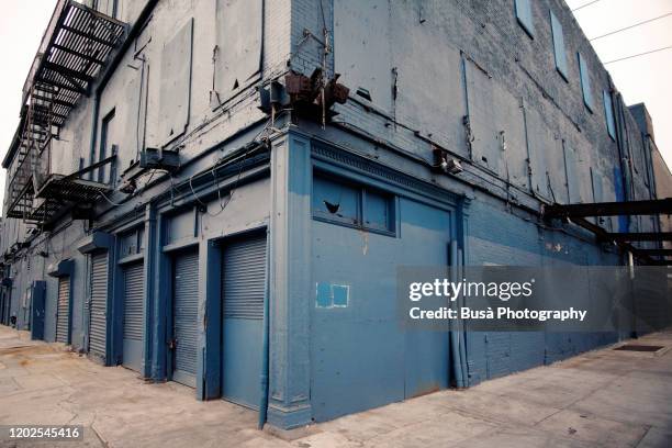 industrial brick building with fire escapes, boarded up windows and metal grates in the meatpacking district, manhattan, new york city - corners stock-fotos und bilder