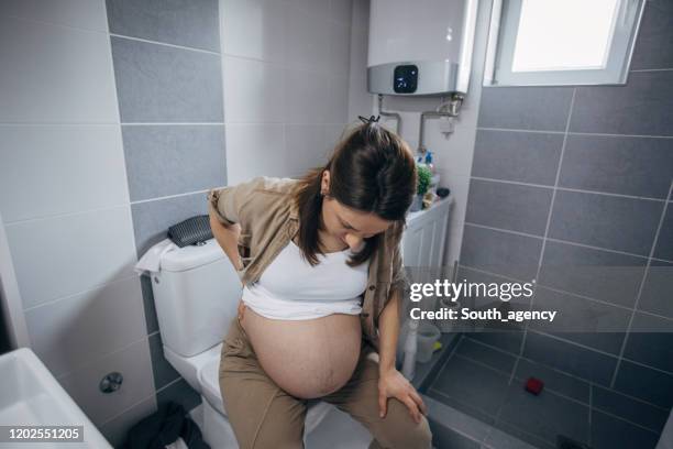 schwangere frau in schmerzen sitzen auf toilette im badezimmer - morning sickness stock-fotos und bilder