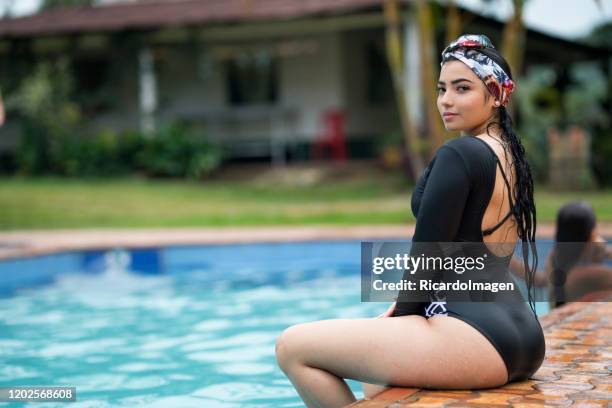 dark-skinned latin woman with black swimsuit is sitting on the edge of the pool looking sideways - dark skin stock pictures, royalty-free photos & images