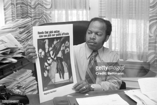 View of American Civil Right leader director of the Voter Education Project John Lewis as he sits at his desk and holds up a voter registration...