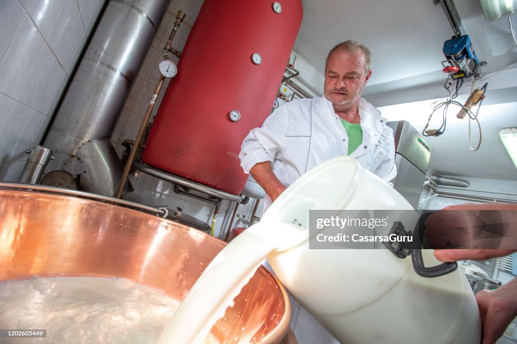 乳酪製造商將新鮮山羊奶倒入不銹鋼加熱元件 - 庫存照片