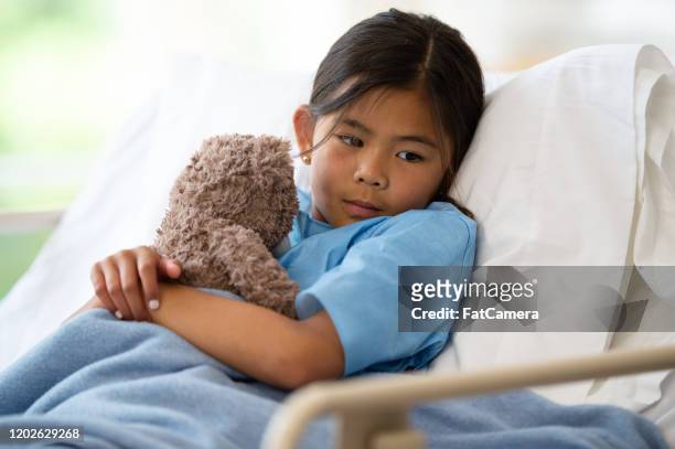 young girl in a hospital bed with her teddy bear stock photo - sad child hospital stock pictures, royalty-free photos & images
