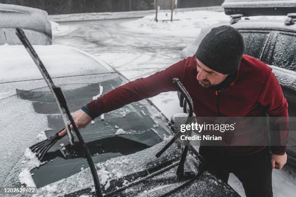 mann reinigt auto-windschutzscheibe vor schnee - eiskratzer stock-fotos und bilder